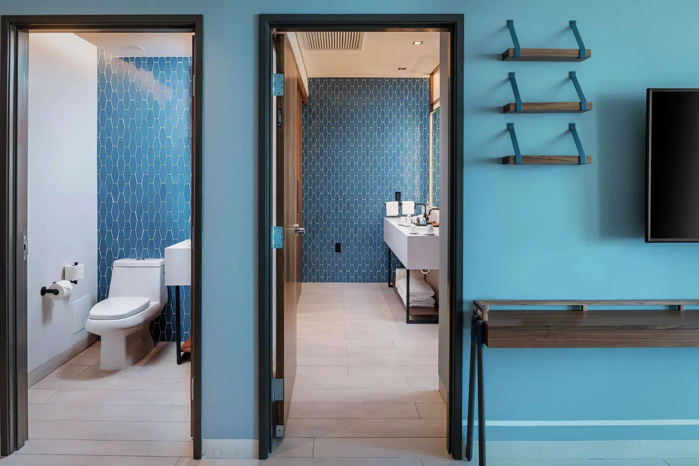 Junior Suite bathroom entrances with blue tile, vanity, and TV wall at Canopy by Hilton Cancun La Isla.