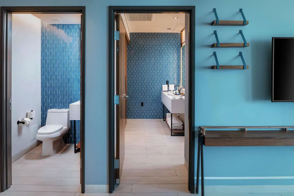 Junior Suite bathroom entrances with blue tile, vanity, and TV wall at Canopy by Hilton Cancun La Isla.