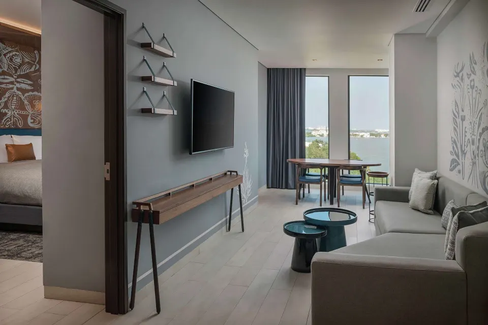 Junior Suite living room with sofa, TV, dining table, and lagoon view at Canopy by Hilton Cancun La Isla.