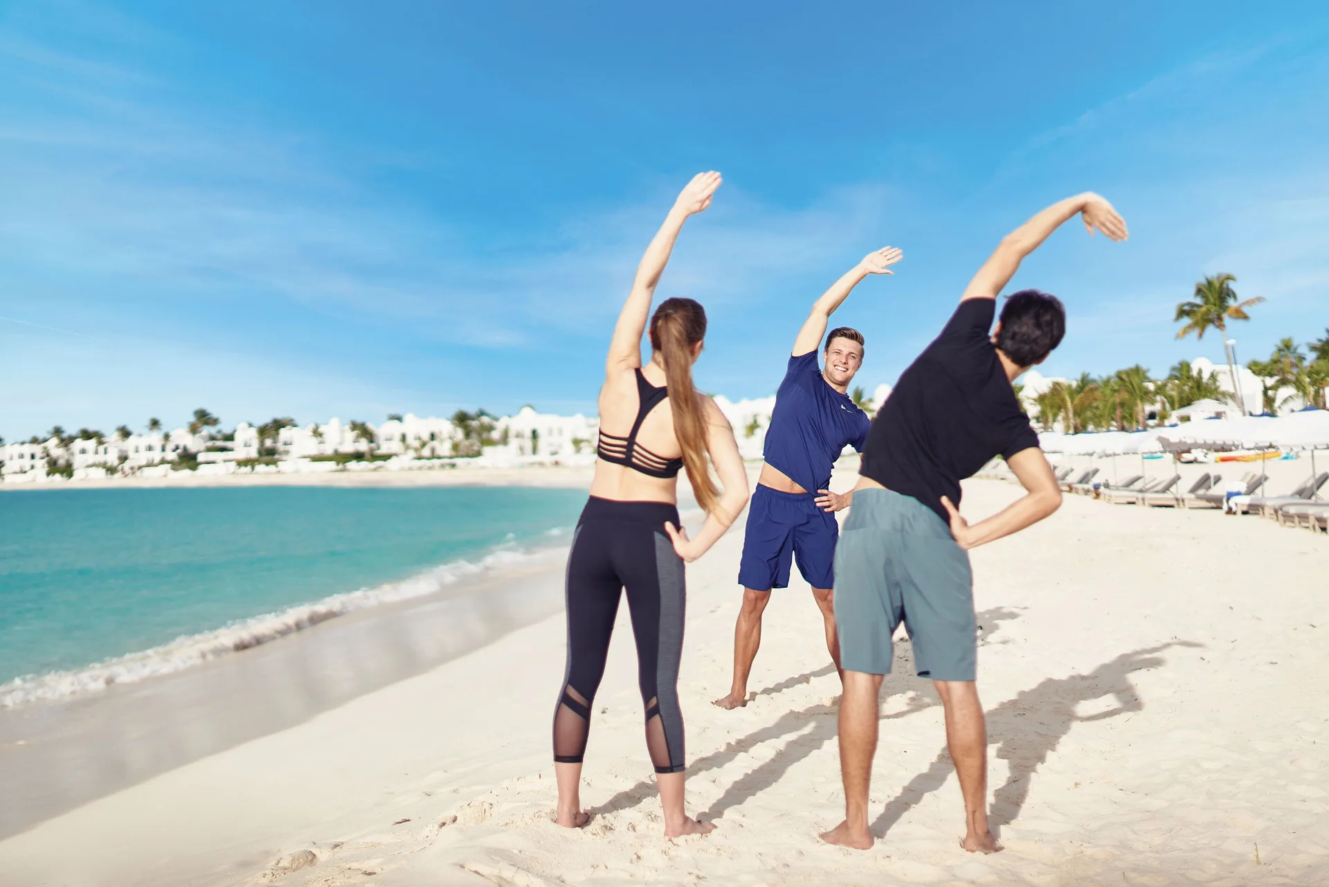 Three guests stretching on the beach at Cap Juluca, Anguilla.