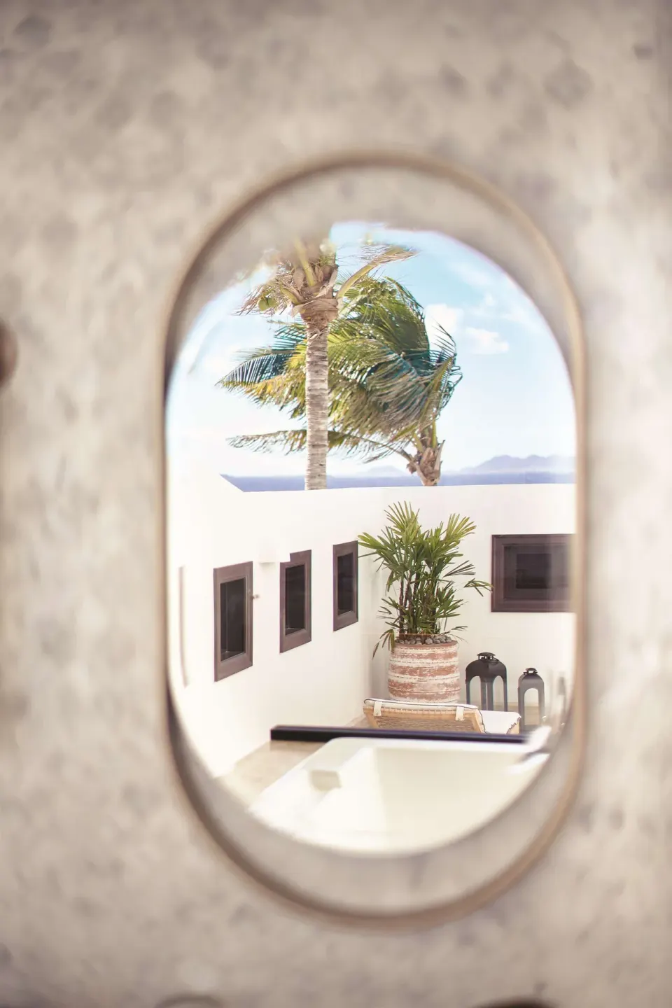 Oval mirror reflecting palms and a white courtyard wall at Cap Juluca, Anguilla.