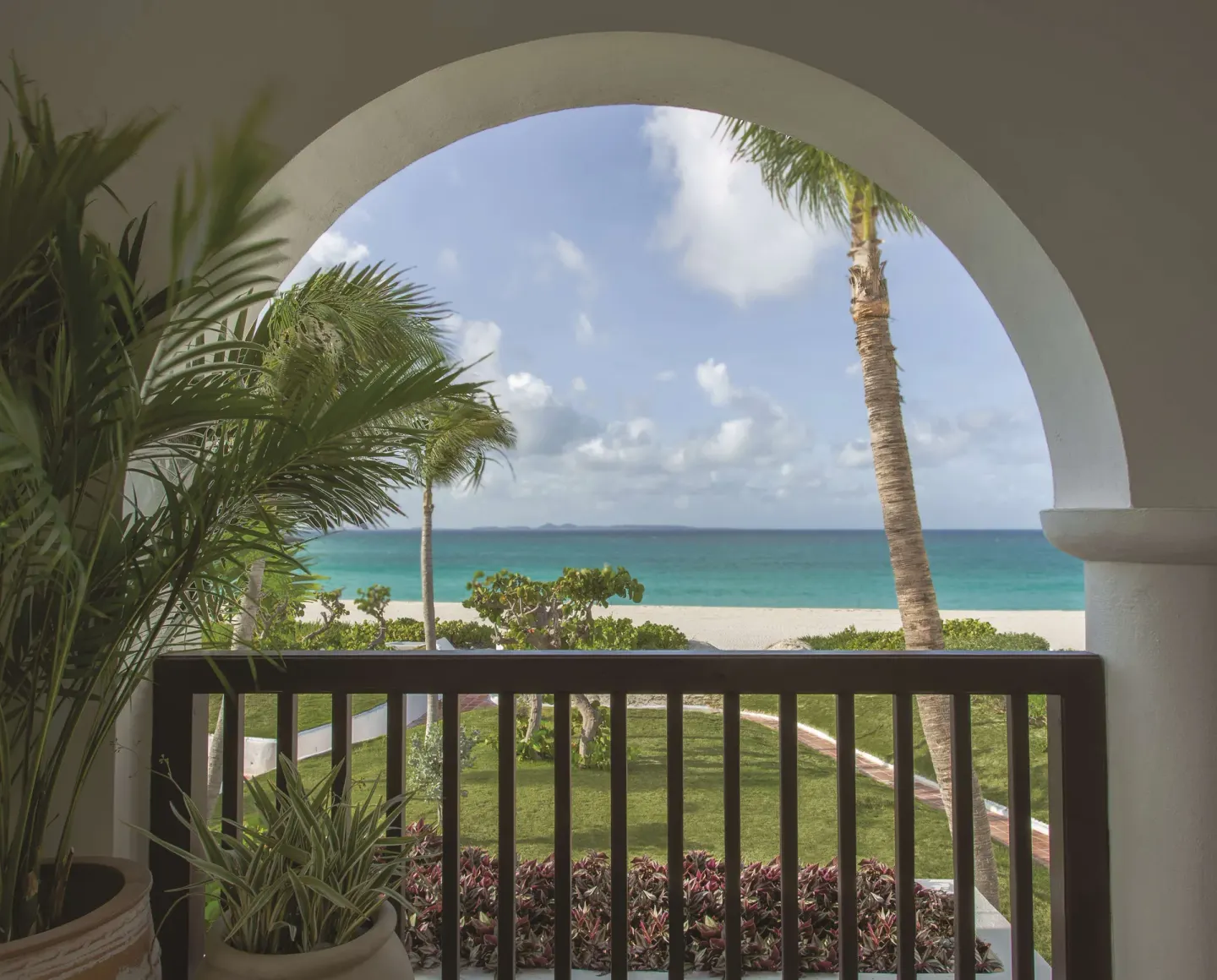 Balcony view from a Deluxe Room, Beachfront at Cap Juluca, Anguilla, framed by palms and an arch.