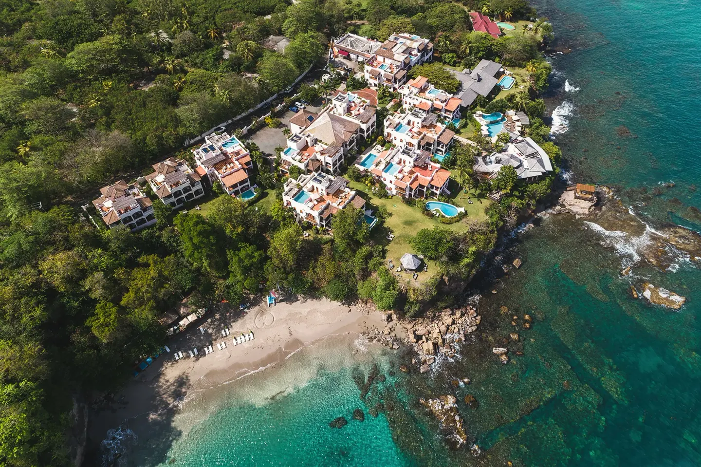 An aerial view shows Cap Maison Resort & Spa above the beach and turquoise sea.