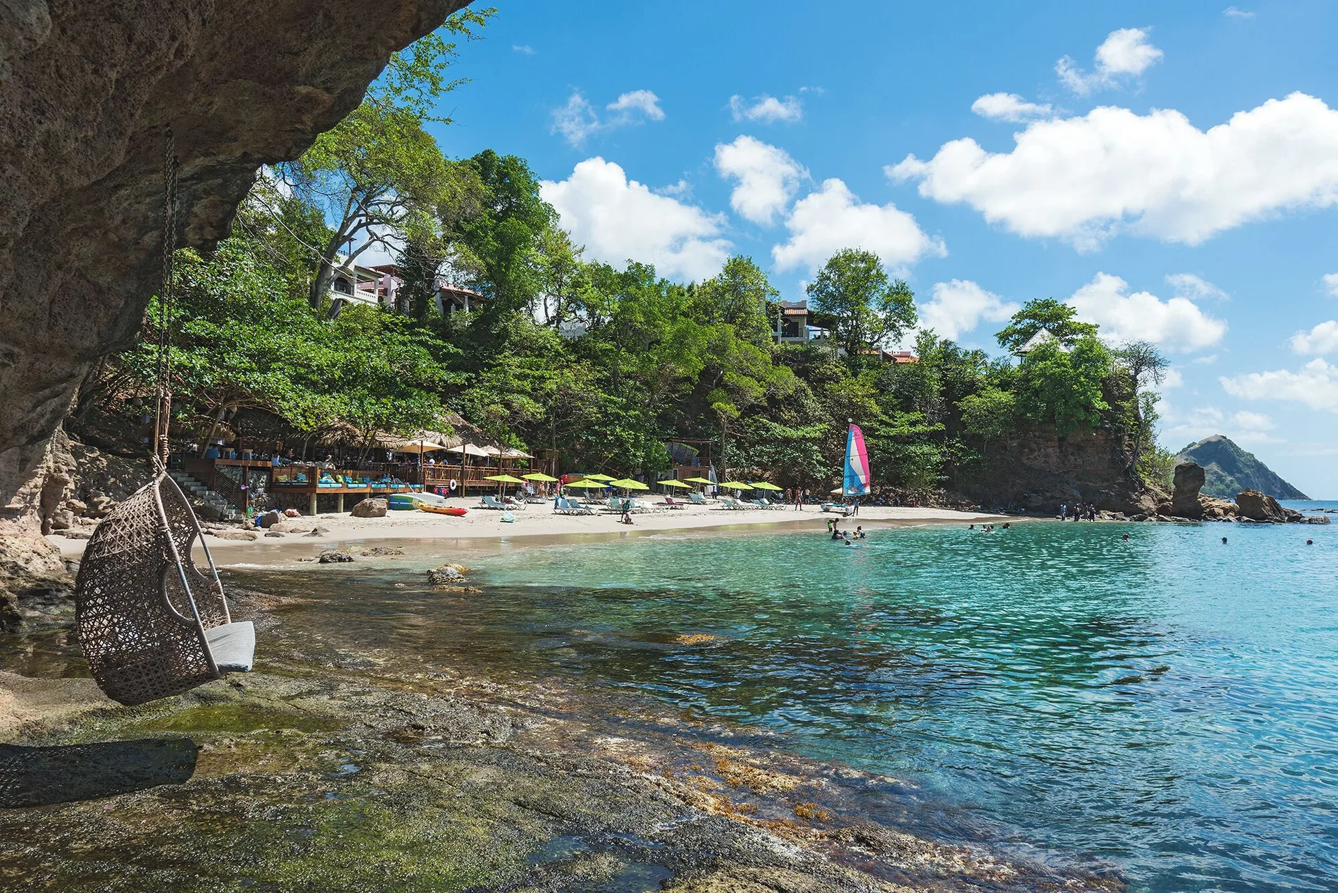 Beach cove with a hanging chair and sailboat at Cap Maison Resort & Spa.