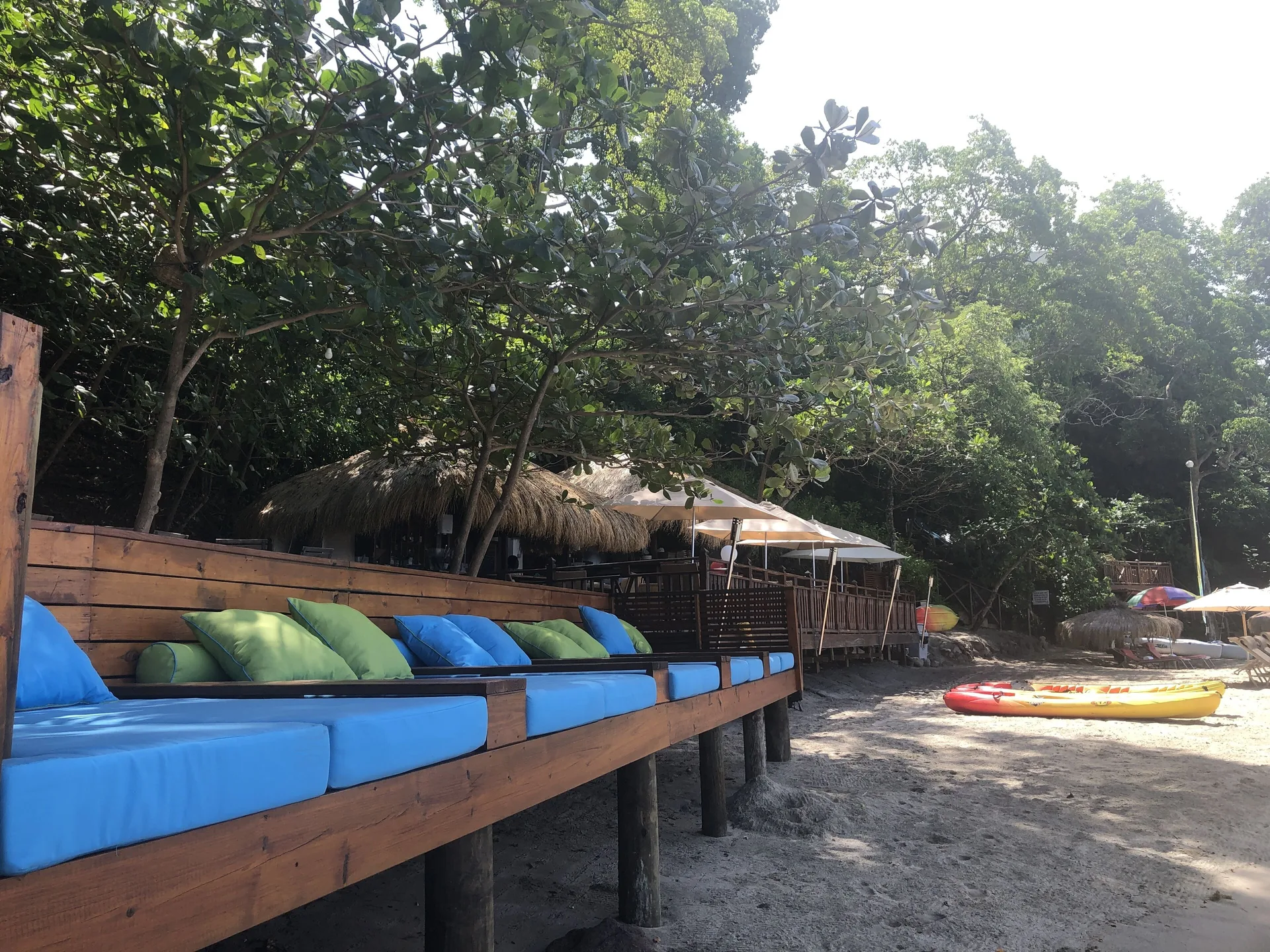 Beach daybeds with blue cushions sit under trees at Cap Maison Resort & Spa.