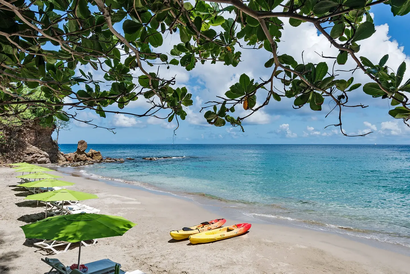 Beach loungers, green umbrellas, and kayaks on the shore at Cap Maison Resort & Spa.