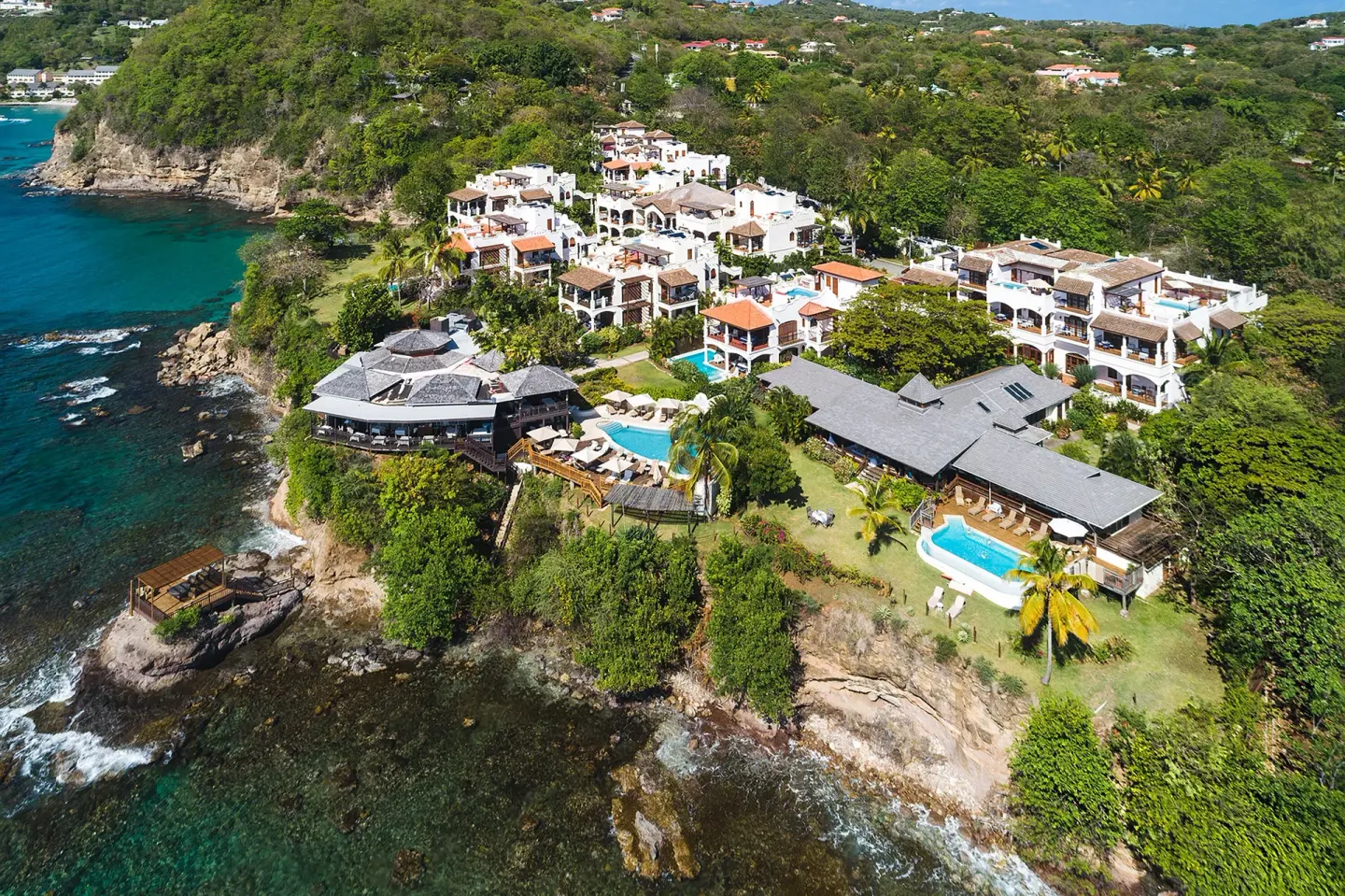 Aerial view of Cap Maison Resort & Spa on a rocky coastline with pools and villas.