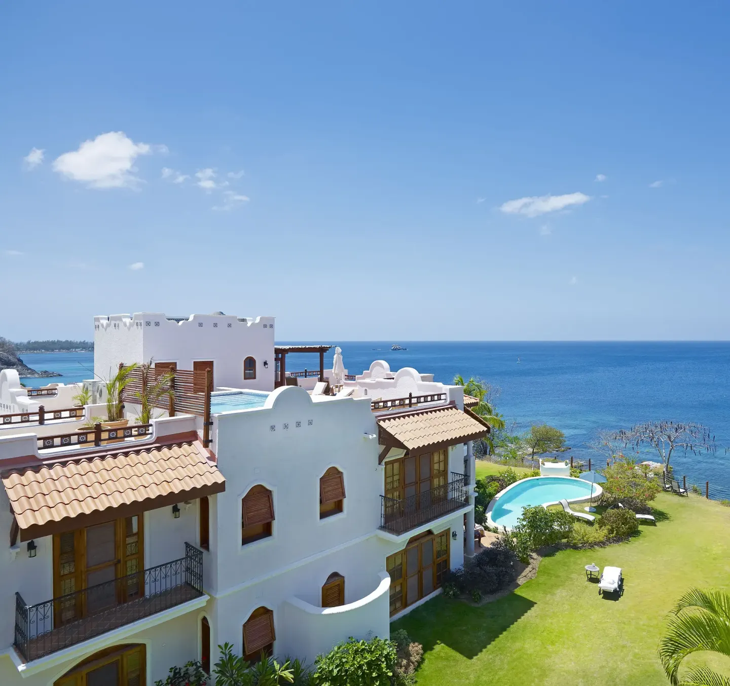 White resort buildings, lawn, pool, and ocean view at Cap Maison Resort & Spa.