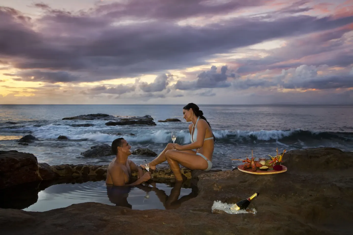 A couple enjoys wine by a rocky sea pool at Cap Maison Resort & Spa.