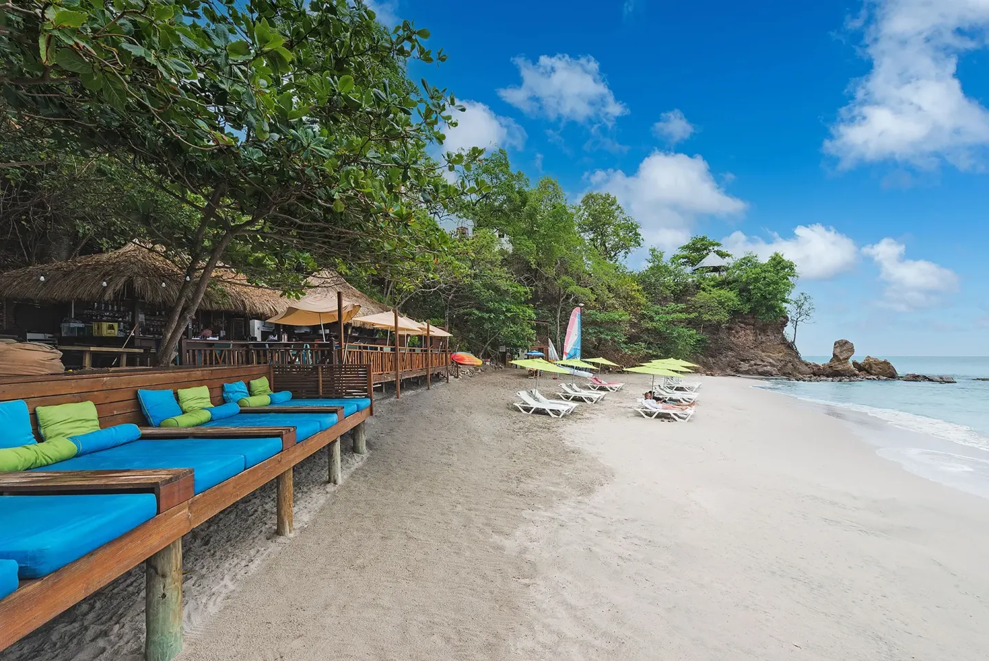A sandy beach with loungers and blue daybeds curves along Cap Maison Resort & Spa.