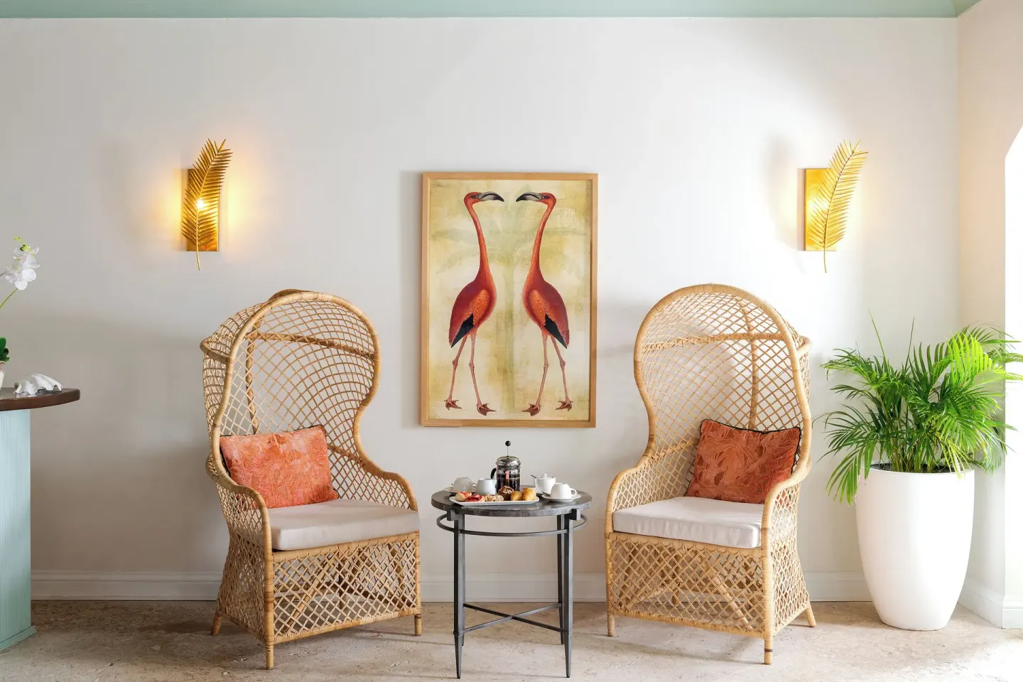 Wicker chairs, flamingo artwork, and tea service in a lounge at Cap Maison Resort & Spa.