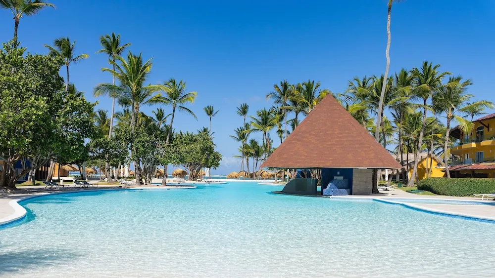 Clear pool with central roofed bar pavilion and palms at Caribe Deluxe Princess.