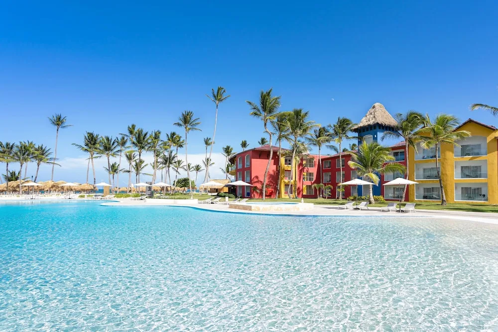 Clear resort pool beside palm trees and colorful buildings at Caribe Deluxe Princess.