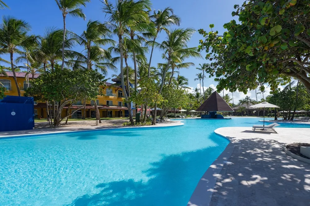 Curving blue pool with palms, loungers and guest buildings at Caribe Deluxe Princess.