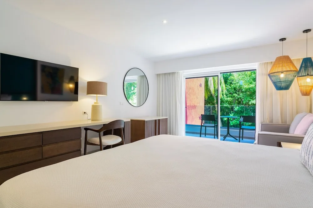 Guest room desk, TV, bed, and balcony seating at Caribe Deluxe Princess.