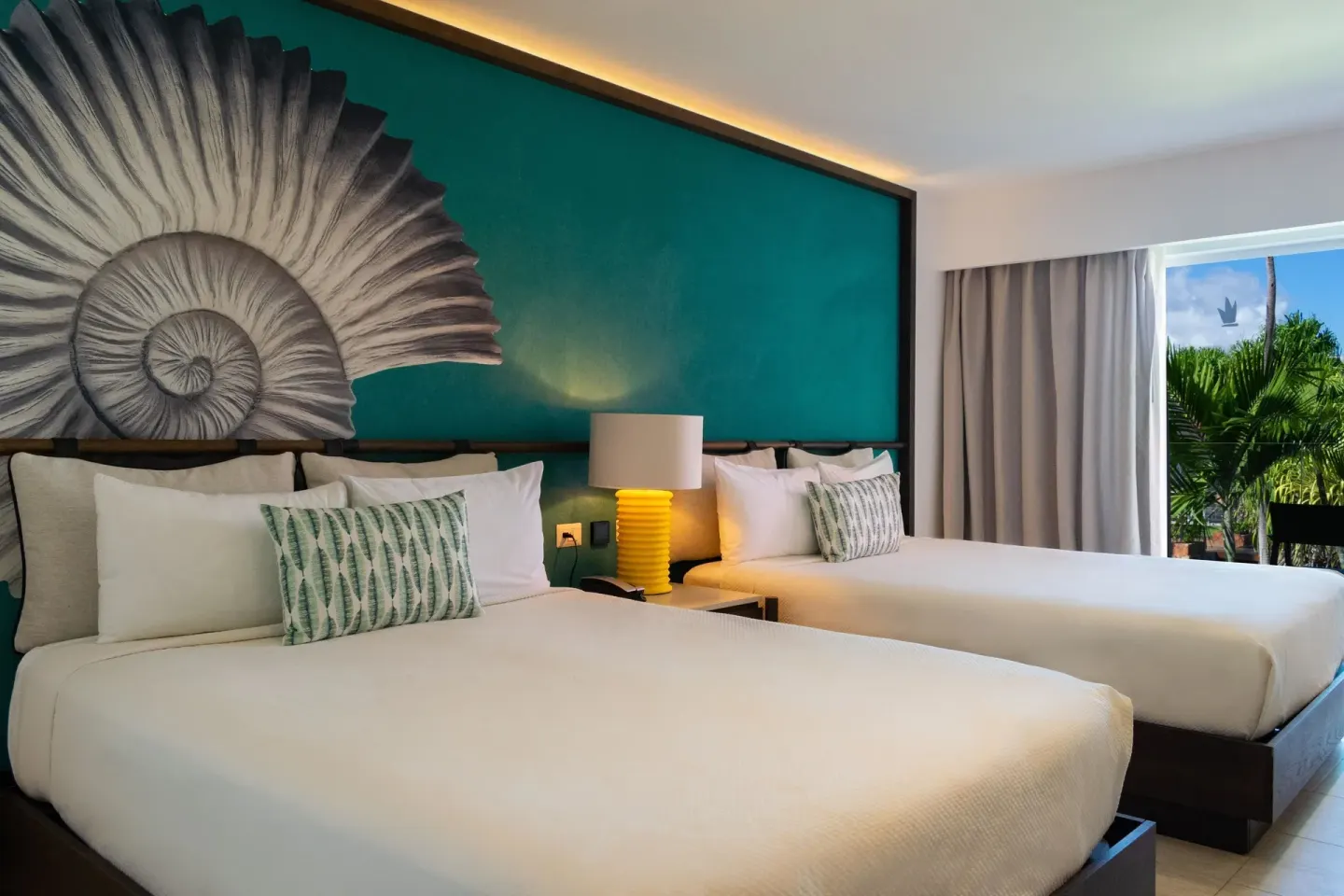 Two-bed guest room with shell mural and window greenery at Caribe Deluxe Princess.