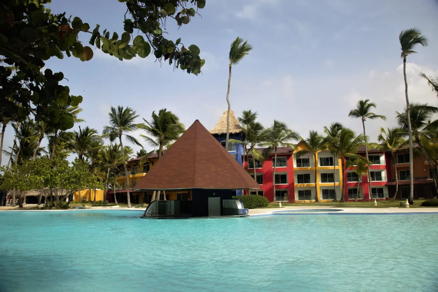 Pool bar pavilion with palms and colorful buildings at Caribe Deluxe Princess.