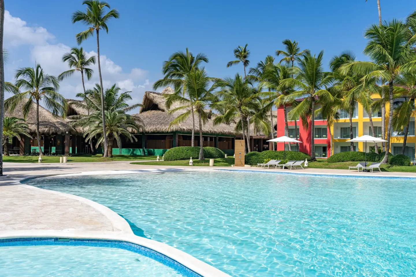 Sunny pool bordered by palms, thatched roofs and guest rooms at Caribe Deluxe Princess.