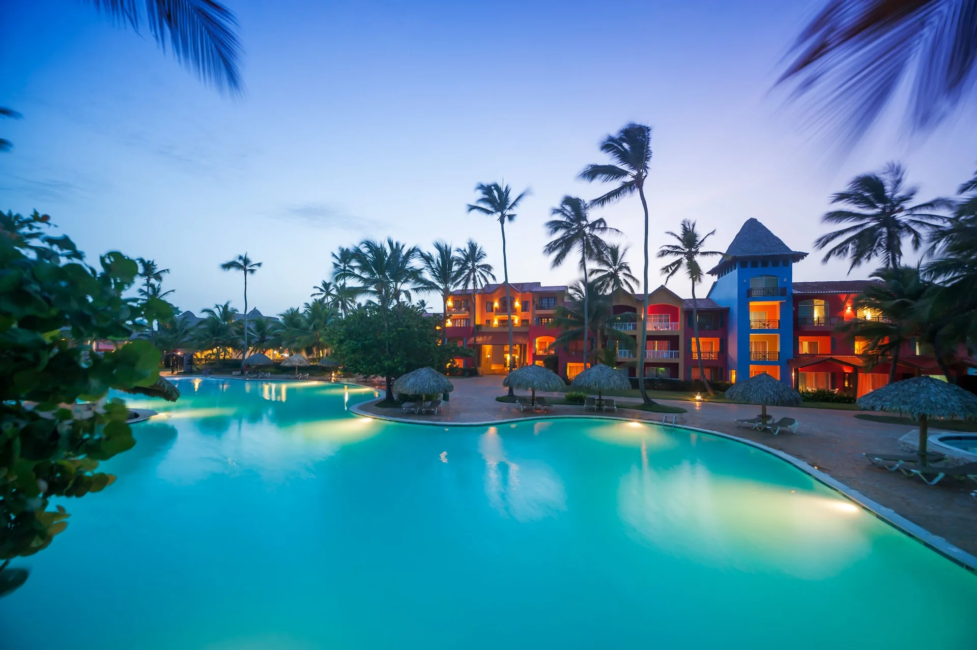 Twilight pool with palms and colorful resort buildings at Caribe Deluxe Princess.