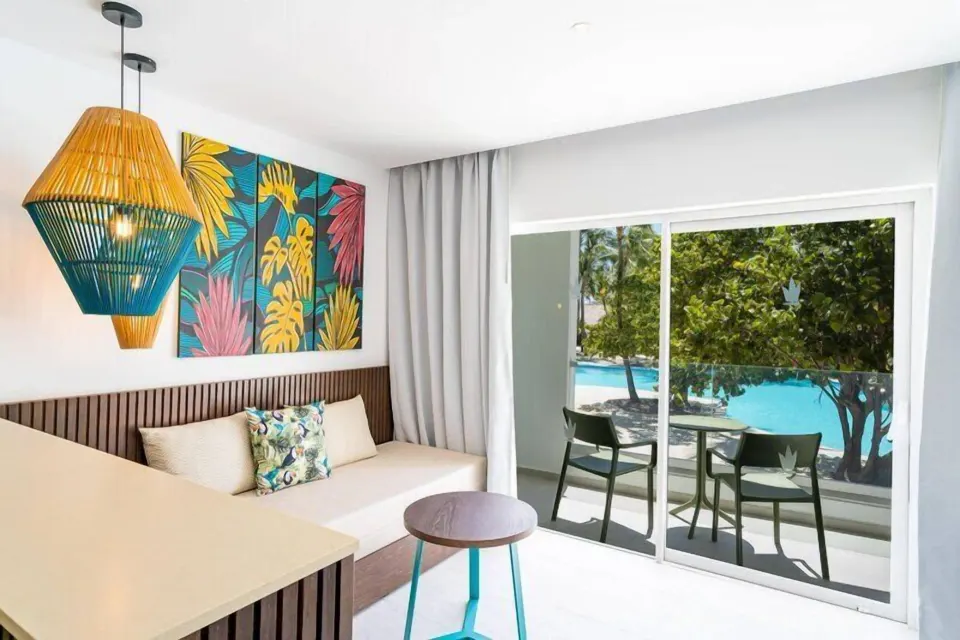 Grand Room at Caribe Deluxe Princess with daybed, balcony seating, and pool visible outside.