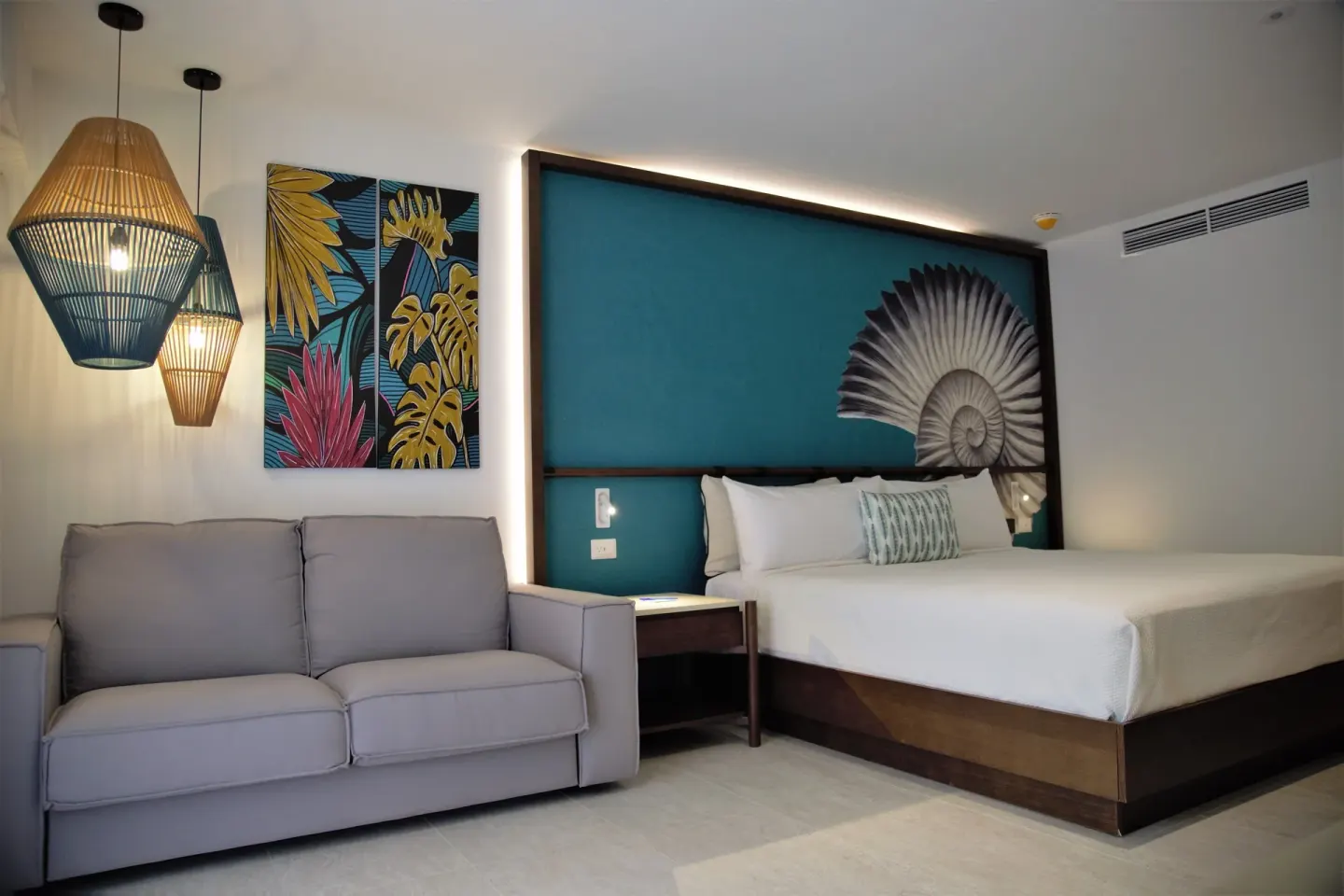 Superior Room king bed with gray sofa and tropical wall art at Caribe Deluxe Princess.