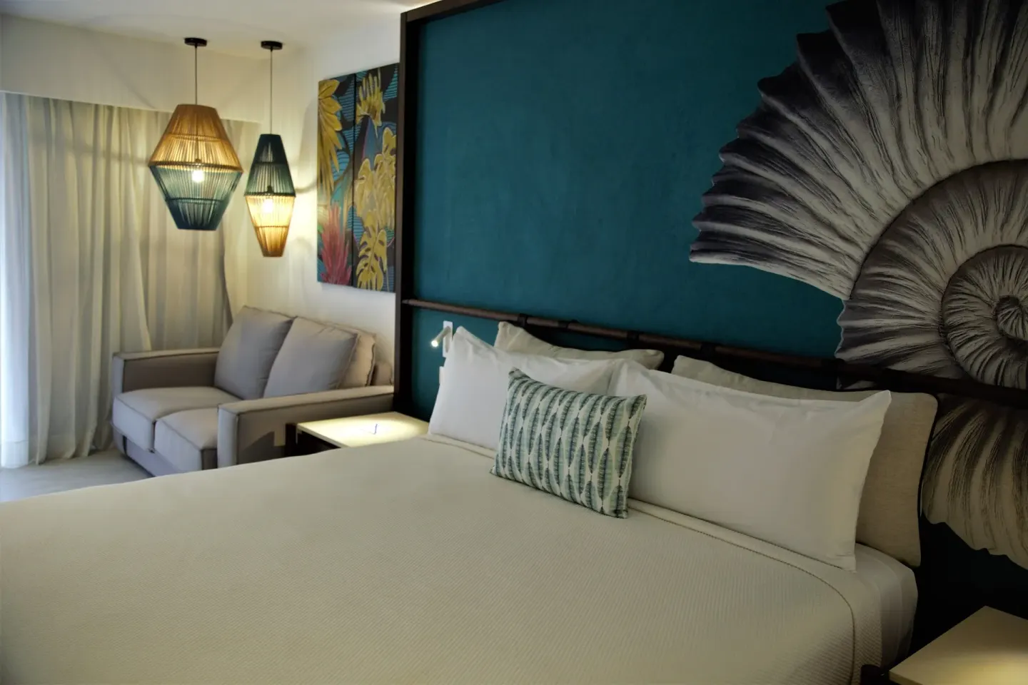 Superior Room king bed beside sofa, curtains and woven pendant lights at Caribe Deluxe Princess.