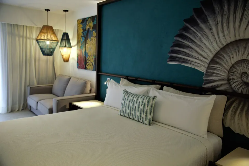 Superior Room king bed beside sofa, curtains and woven pendant lights at Caribe Deluxe Princess.