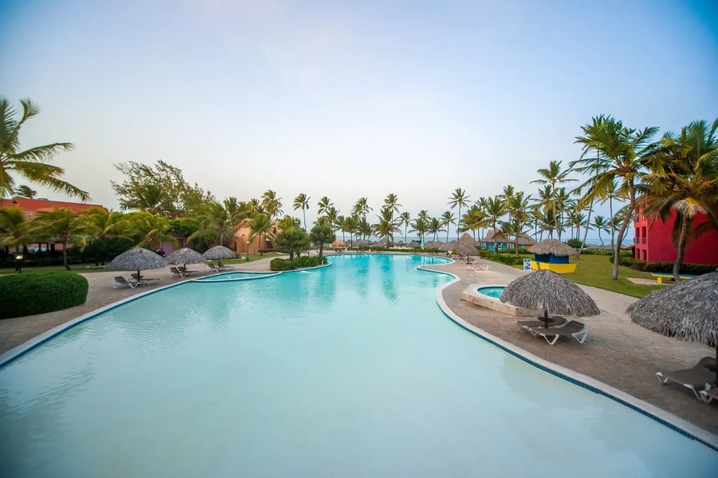 Large resort pool with palms near guest room buildings at Caribe Deluxe Princess.