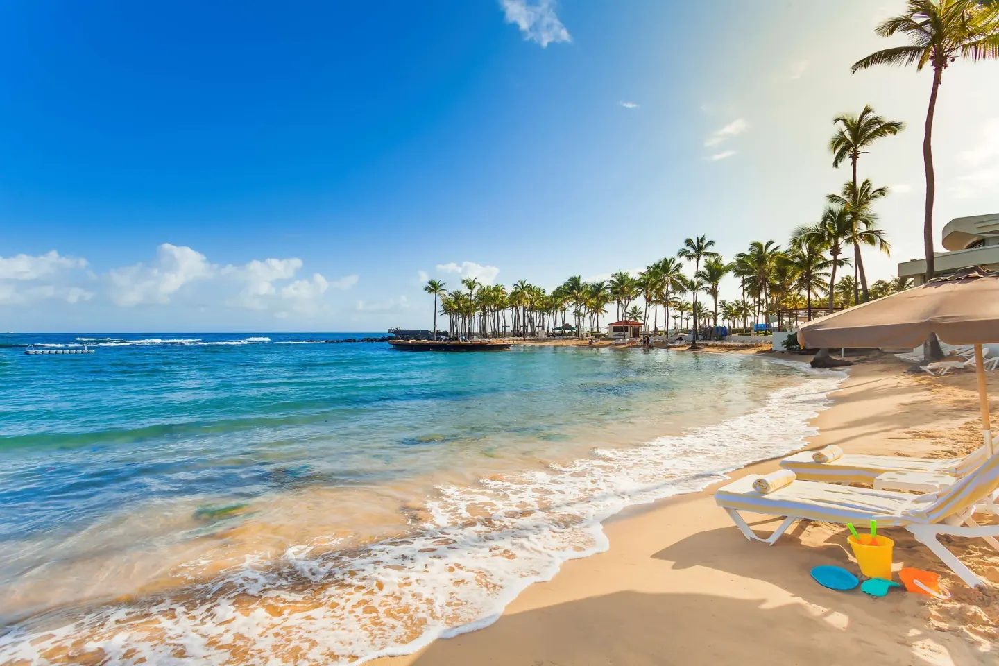 Sandy beach at Caribe Hilton with lounge chairs, umbrellas, palms, and clear water.