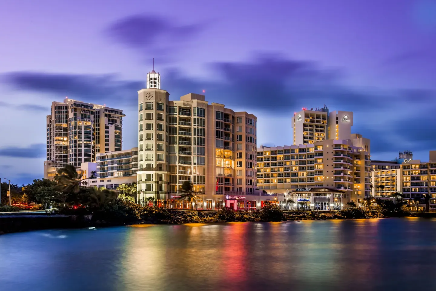 Caribe Hilton buildings lit at dusk across the water.