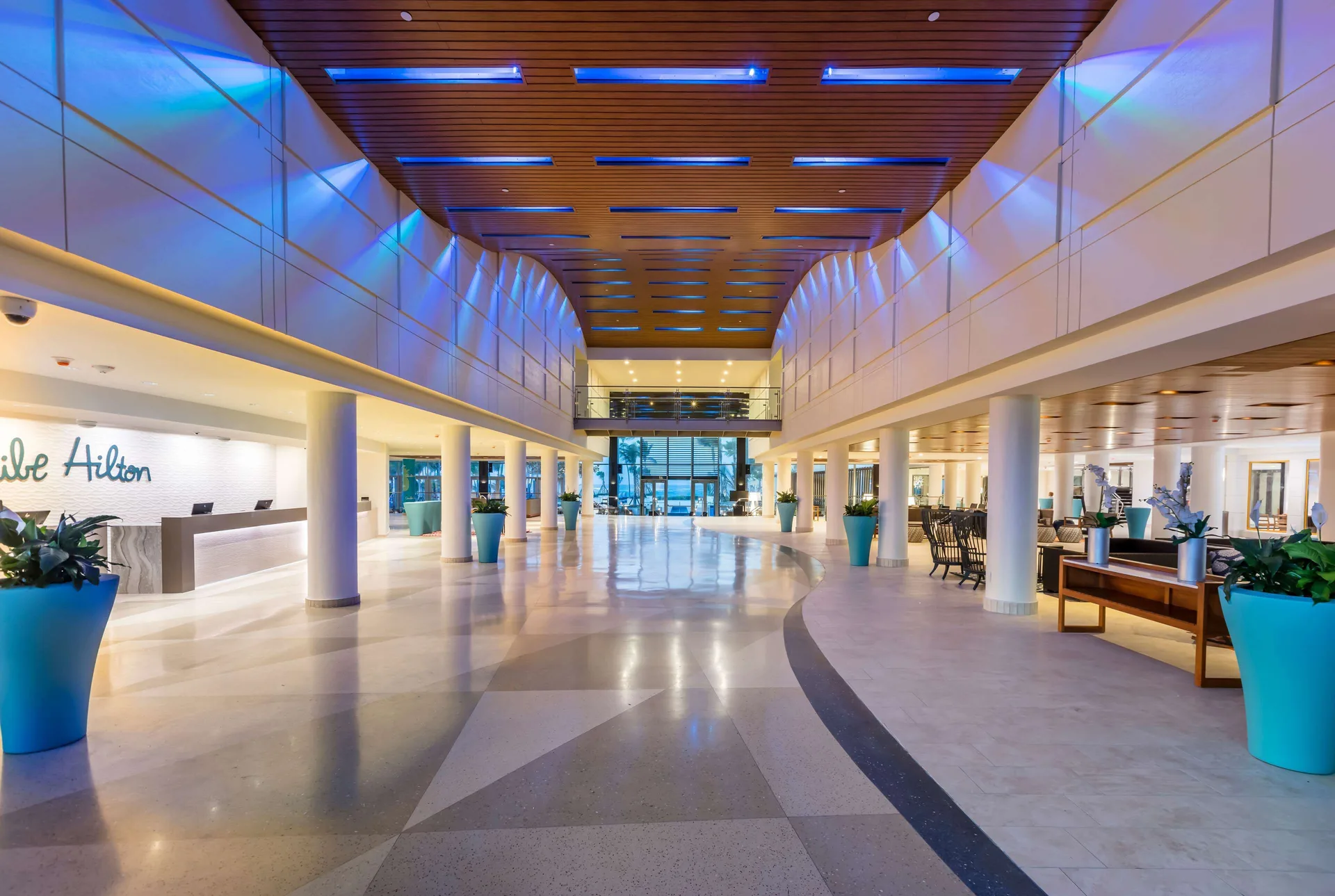 Spacious lobby with reception desk, columns, blue ceiling lights, and planters at Caribe Hilton.