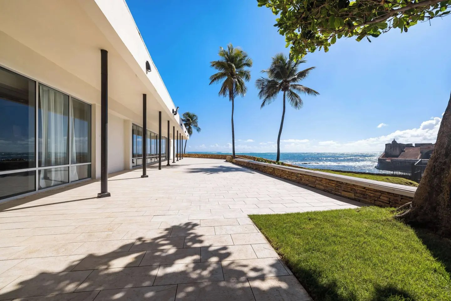 Oceanfront terrace with palms and historic fort views at Caribe Hilton.
