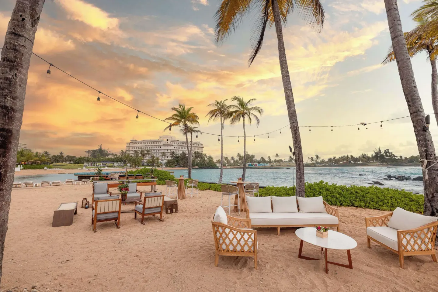 Beach lounge seating under palms at sunset at Caribe Hilton.
