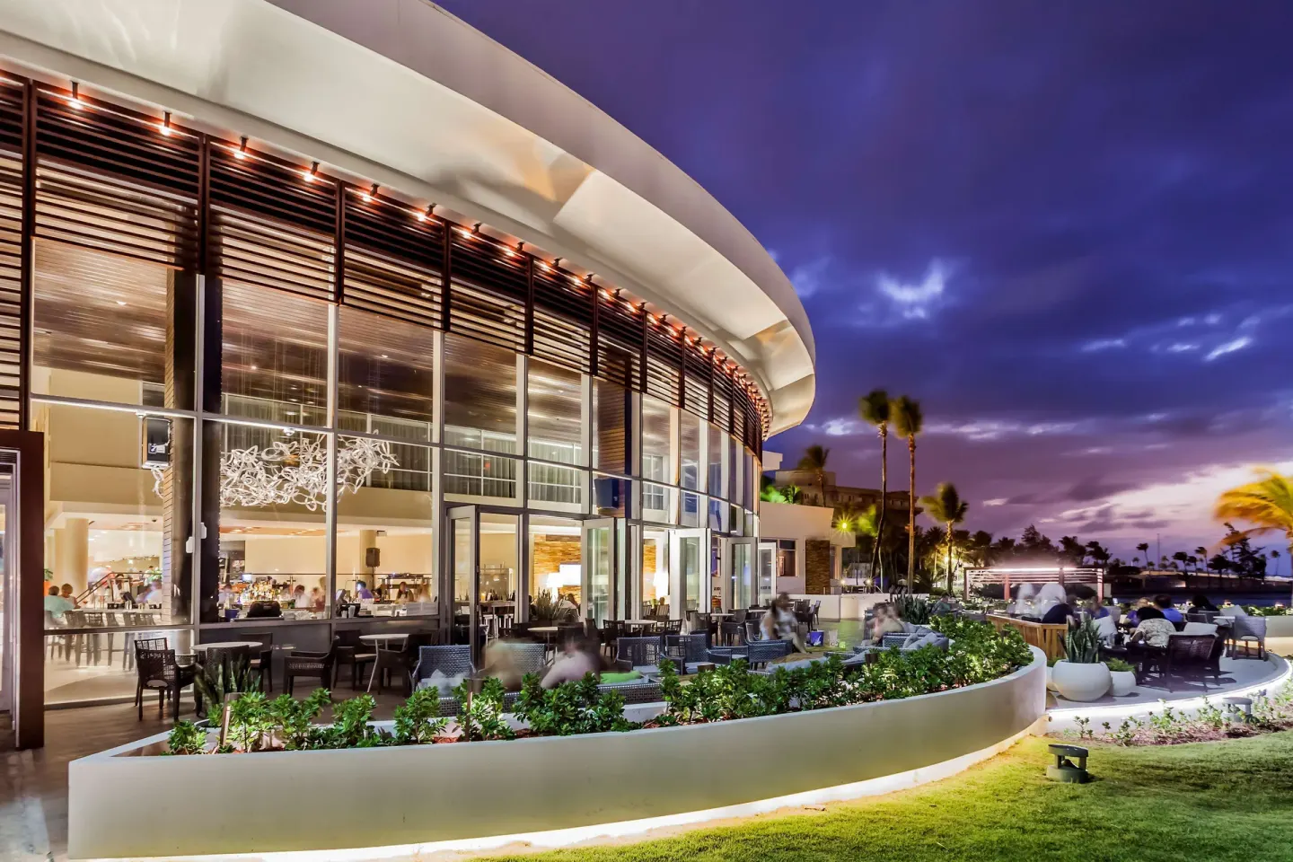 Curved glass lounge terrace with outdoor seating at dusk at Caribe Hilton.
