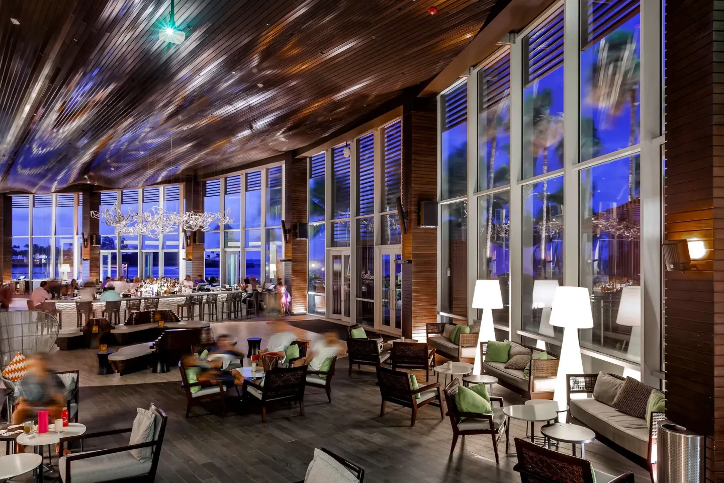 Evening bar lounge with wicker seating and tall blue-lit windows at Caribe Hilton.