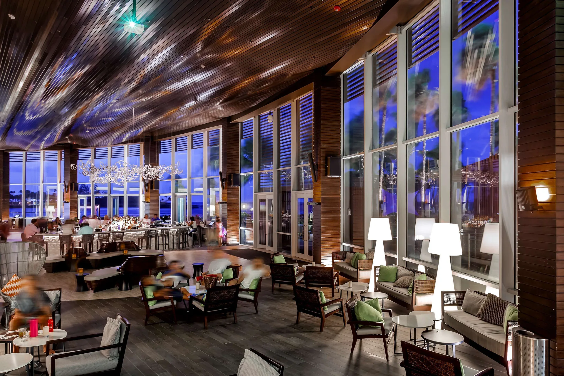 Evening bar lounge with wicker seating and tall blue-lit windows at Caribe Hilton.