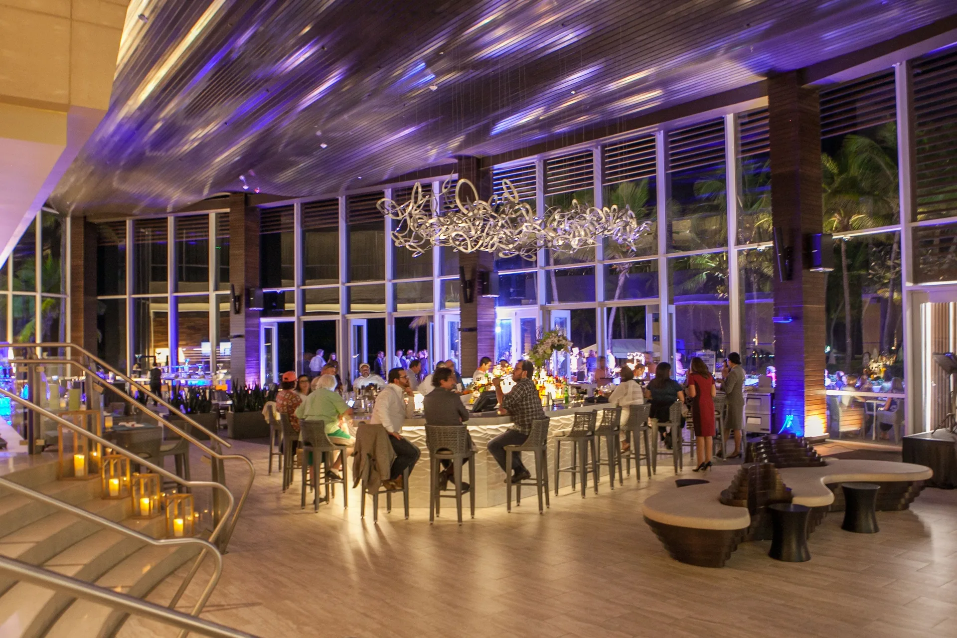 Guests sit around a glowing lobby bar with tall windows at Caribe Hilton.