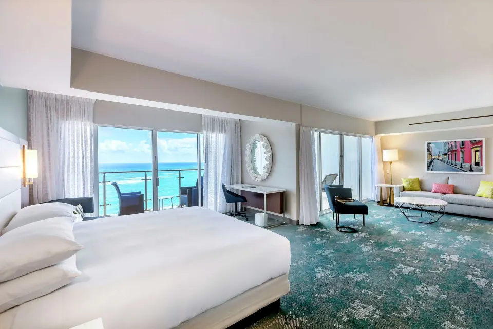 King bedroom with ocean-facing balcony and sitting area in a suite at Caribe Hilton.