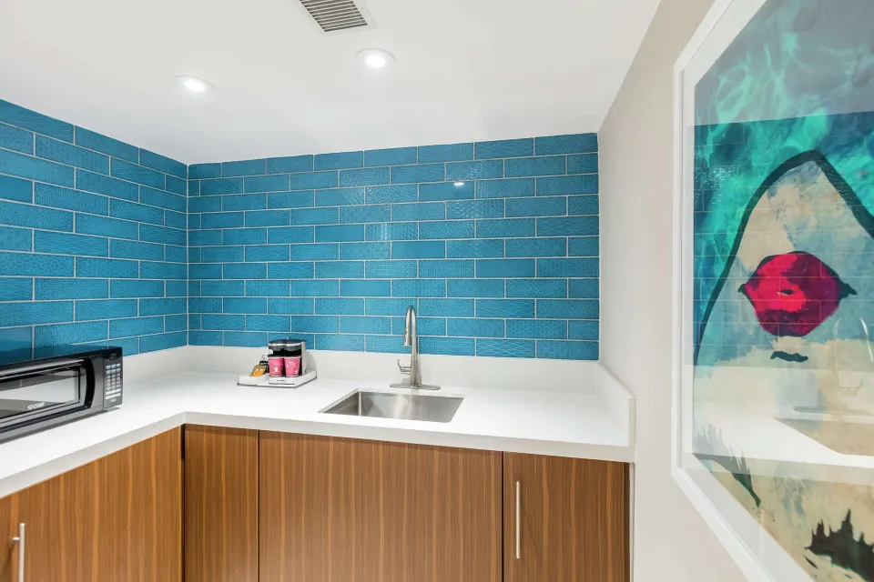 Suite kitchenette with blue tile backsplash, sink, microwave, and artwork at Caribe Hilton.