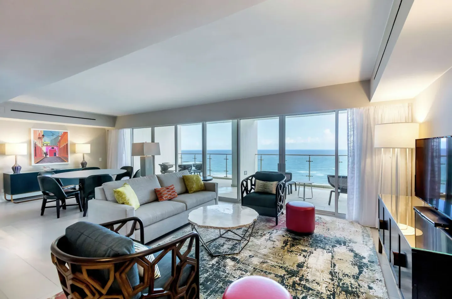 Living room with ocean-view balcony, sofa, dining table, and TV at Caribe Hilton.