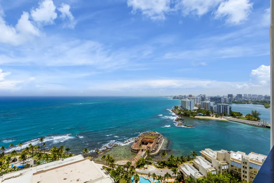 Ocean and coastline view from a two-bedroom bi-level suite at Caribe Hilton with historic fort below.