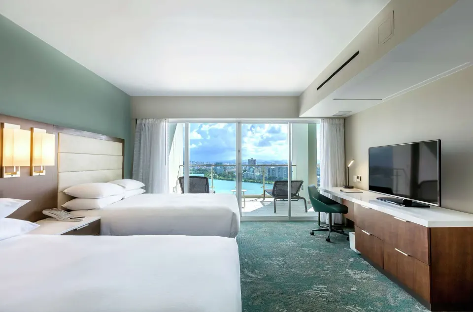 Bedroom with two double beds, balcony, desk, and TV at Caribe Hilton.