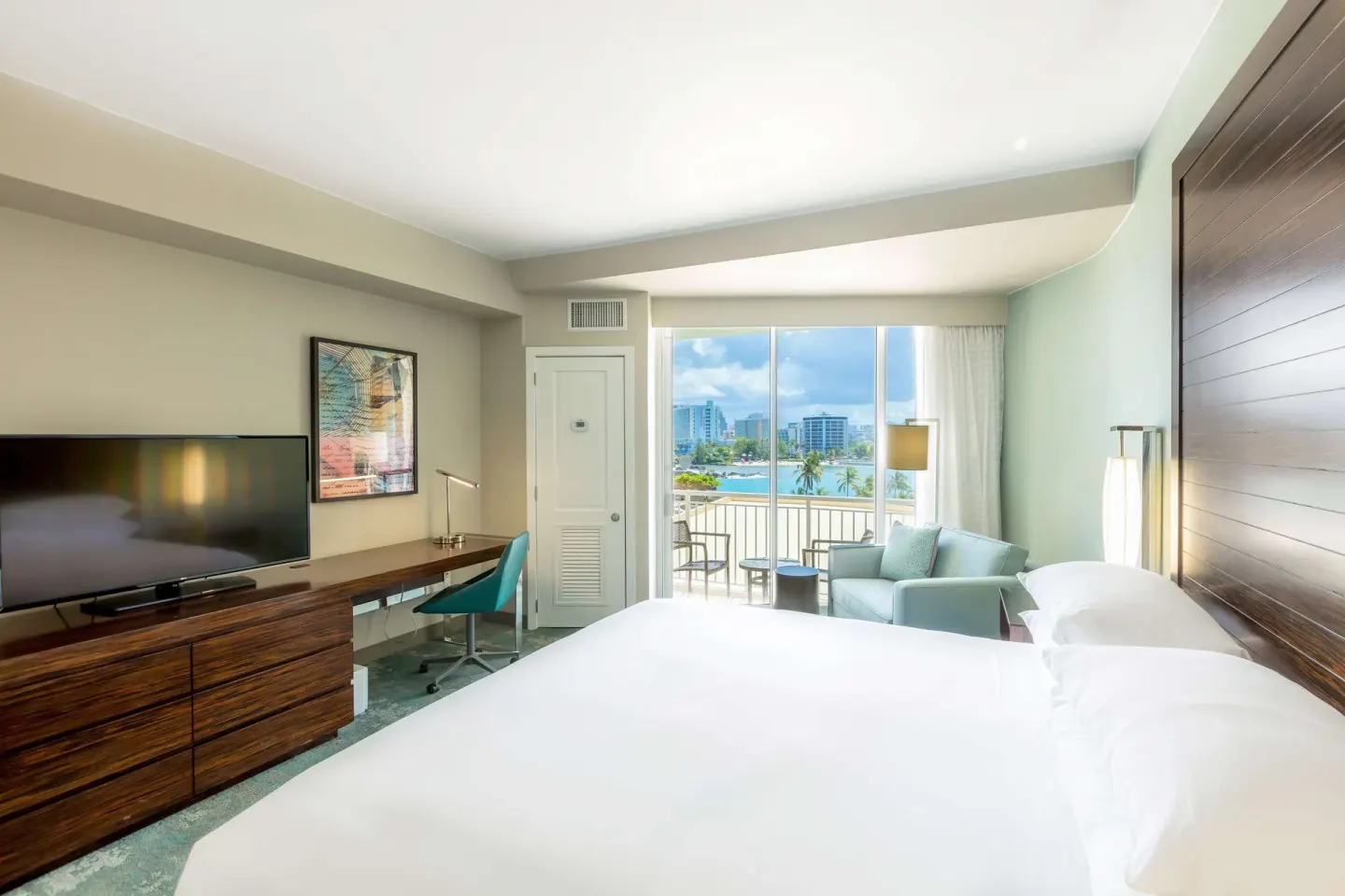 King guest room with TV, desk, balcony, and water view at Caribe Hilton.