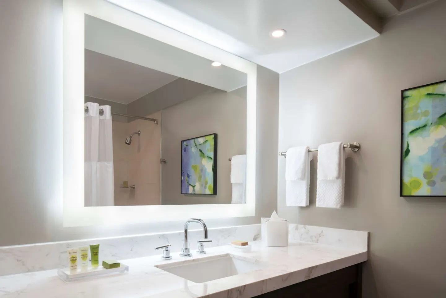 Bathroom vanity with lit mirror, towels, and shower reflection in a Caribe Hilton guest room.