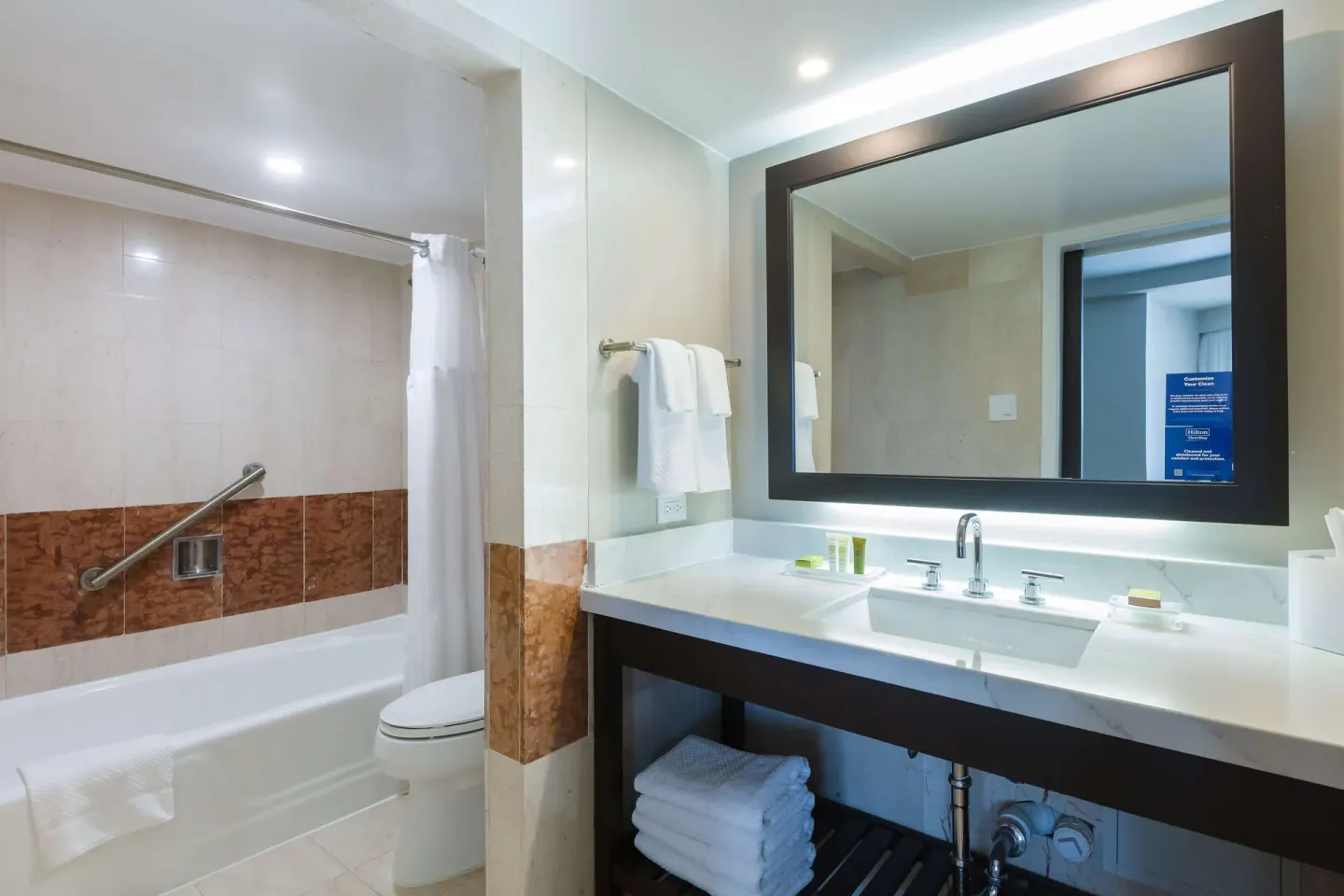 Bathroom with vanity, mirror, tub, and shower curtain in a Caribe Hilton guest room.