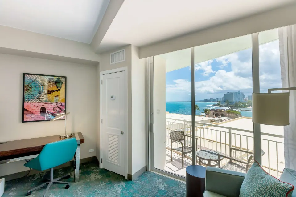 Desk, chair, seating area, and balcony ocean view in a Caribe Hilton guest room.