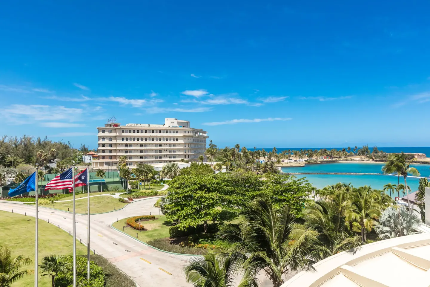Resort and ocean view from a guest room at Caribe Hilton with palms, flags, and blue water.