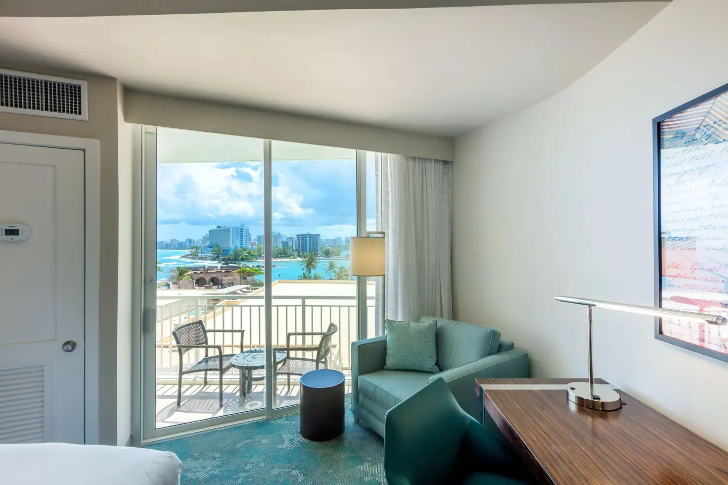 Sofa, desk, and balcony seating in a Caribe Hilton guest room with water views.
