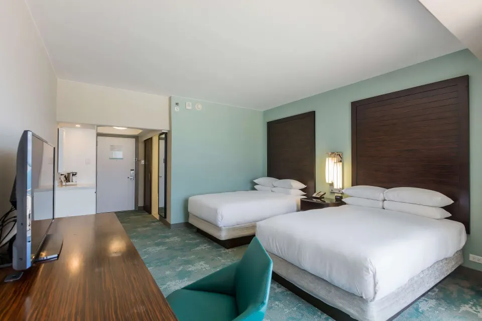 Two double beds, desk, TV, and entry area in a Caribe Hilton guest room.