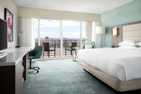 King guest room with desk, balcony chairs, and bright windows at Caribe Hilton.